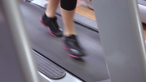 Sport, fitness, lifestyle, technology and people concept - close up of woman legs walking on treadmills in the gym.