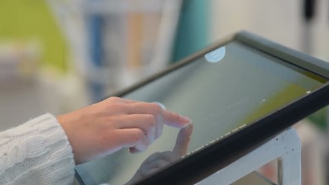 Close-up shot of woman customer using touchscreen computer to look through electronic catalogue in the store