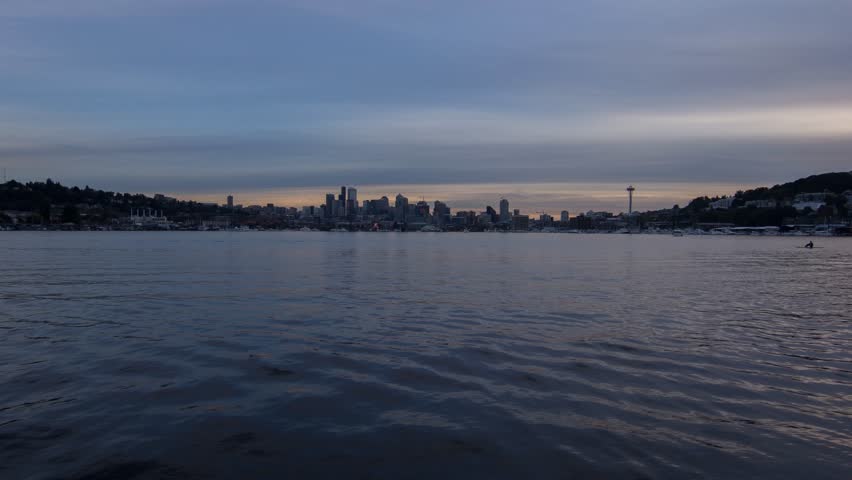 A wide view of the Seattle Skyline lighting up at night as seen from Lake Union