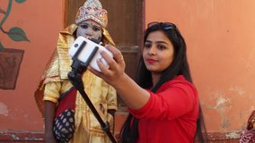 Indian traveller taking selfies with girls dressed as Hindu goddess with make-up and traditional clothing at the Pushkar Mela festival in Rajasthan, India 