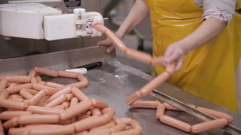 Food factory. Worker produces sausages on a automated food production equipment.