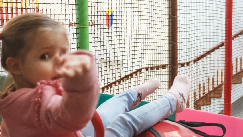 the little girl on the tubing rolls with slides in the play area.