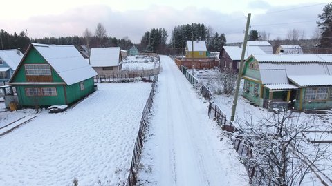 Camera flying over winter rural road in Russian village. Summer timber houses with land lots are covered with snow. Karelia, north of Russia