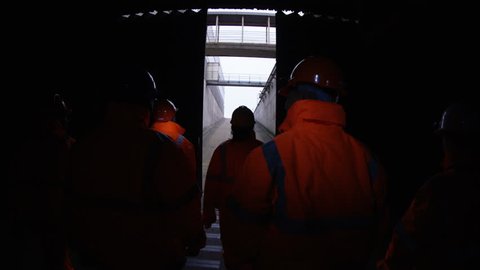 4K Workers at a fuel plant walking into the light