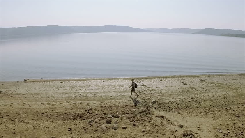 Aerial. One Man traveler goes on  coastline of  lake. Circular flight