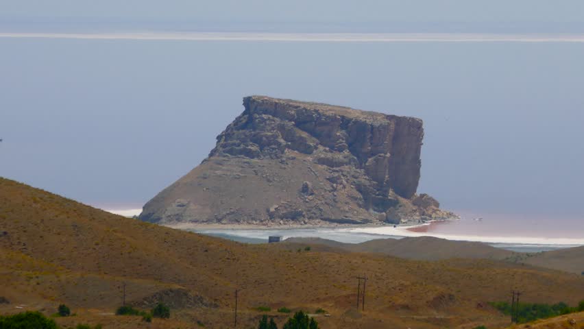 Aerial long shot of a rock hill near crystal salt rock salty beach shore of a red pink sea