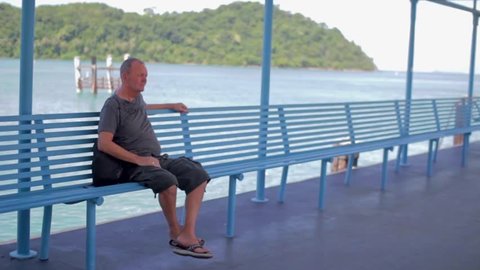 a man sits on a blue bench on the sea pier