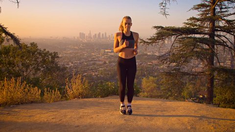 Fit woman warming up before her morning jog. The skyline of Los Angeles can be seen in the background. Slow Motion.