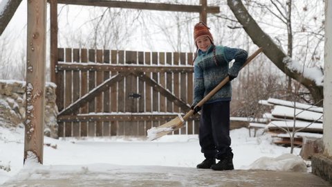 Boy removes snow shovel near the house. Cleaning snow in the winter near the house. The child cleans shovel the snow covered track.  
