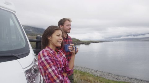 Travel couple by mobile motor home RV campervan. Travelers relaxing camping and enjoying traveling on Iceland in recreational vehicle. Man and woman enjoying coffee in Icelandic nature landscape.