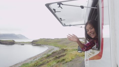Travel woman in mobile motor home RV campervan waving hand saying hello hi looking out window of car on Iceland in recreational vehicle. Girl enjoying coffee in Icelandic nature landscape.