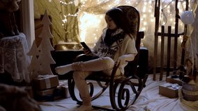 Beautiful Little Girl is Sitting in the Rocking Chair and Use Mobile Phone