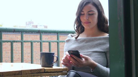 Plus size model woman having coffee and checking her phone on balcony of her apartment