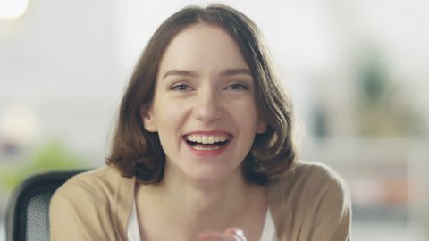 Beautiful Young Woman Laughs on the Camera. Her Background is Bright and Blurred. Shot on RED Cinema Camera in 4K (UHD).