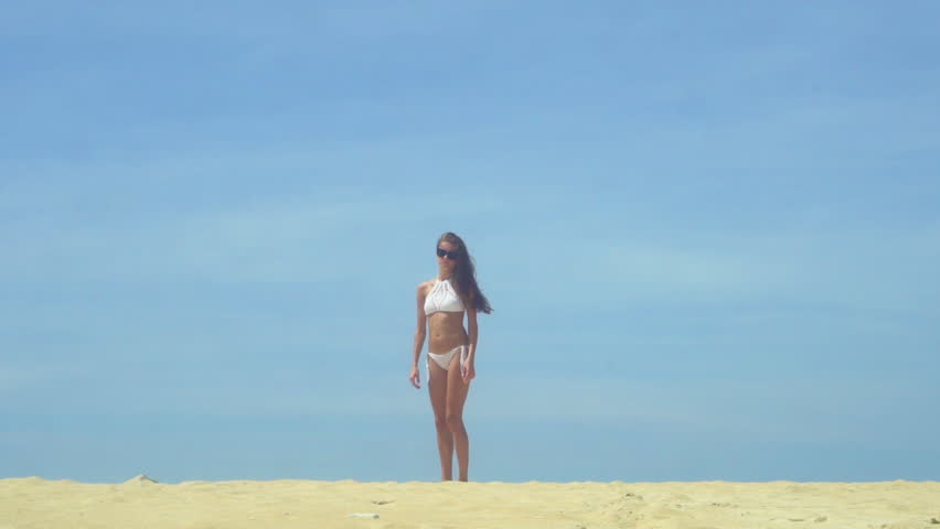 Slow motion shot of a happy girl jumping on the beach with blue sky on the background