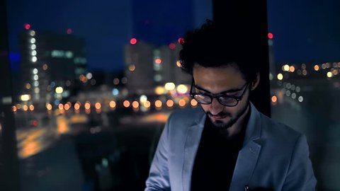 Young businessman looking at tablet by background of the night city. Slow motion.