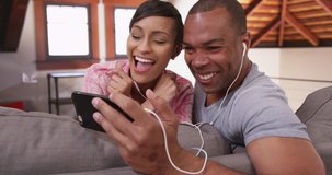 An African American couple sing along to a song on their smart phone. A black man and woman have fun singing along while sitting on their couch. 4k