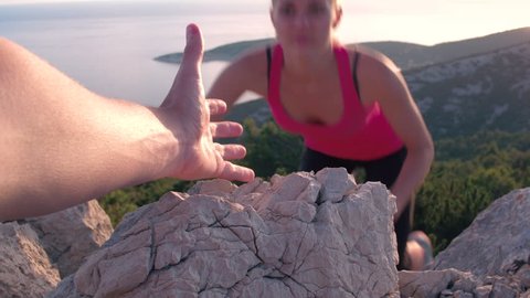 Closeup of a male's hand stretching out and helping female friend reach the mountain top by pulling her up. POV of a man giving hand to a woman climbing on the mountain and helping her reach the top