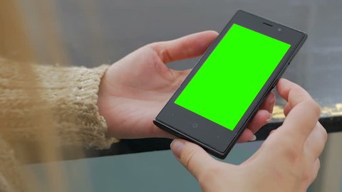 Woman looking at vertical smartphone with green screen. Close up shot of woman's hands with mobile