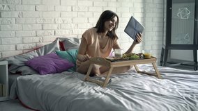 Woman chatting on tablet computer during breakfast sitting on bed at home
