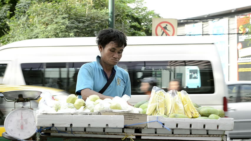 BANGKOK - CIRCA MAY 2012: Man selling fruit from a cart on the sidewalk near a