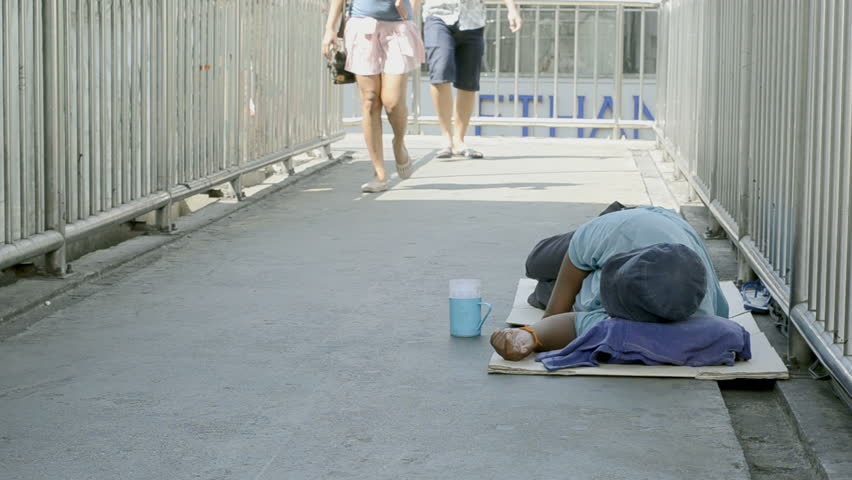 BANGKOK - CIRCA MAY 2012: Beggar lying down on a footbridge, while people pass
