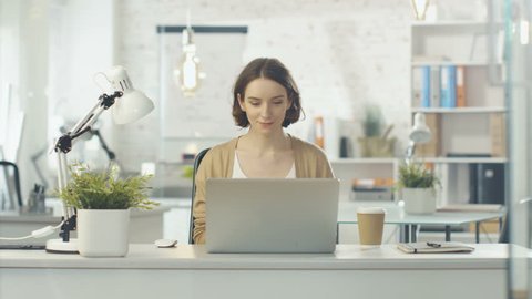 Portrait Shot of a Creative Woman Sitting at Her Desk. Using Notebook. She Sits in a Light and Modern Office. Shot on RED Cinema Camera in 4K (UHD).