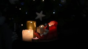 Video of beautiful lighted Christmas candles and a tiny sleeping Santa statuette, in front of the Christmas tree, selective focus