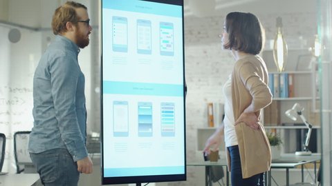 Young Coworkers Discuss Charts Drawn on Their Electronic Whiteboard. Their Office is Stylish and Modern Looking. Shot on RED Cinema Camera in 4K (UHD).