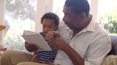 Grandfather And Grandson Reading Book At Home Together
