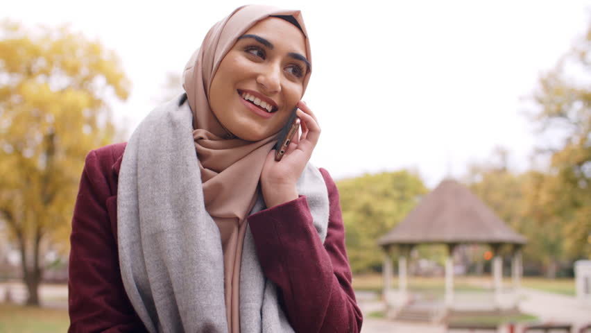 British Muslim Woman Using Mobile Phone In Park 