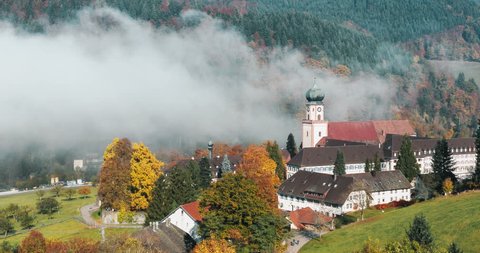 Peaceful autumn mountain landscape with a historic monastery covered in fog.  View over St. Trudpert Abbey in Germany, Black Forest. Scenic 4k time lapse. 