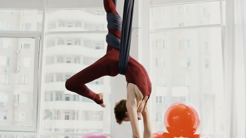 Focused pretty mature woman doing aerial yoga in gym
