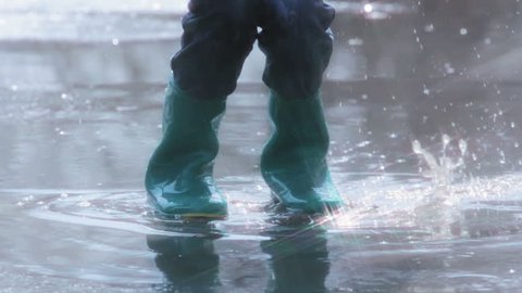 Slow motion of a child in rubber boots jumping in the middle of the puddle