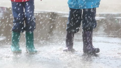 Boy and girl having fun on a rainy day jumping and dancing in puddle