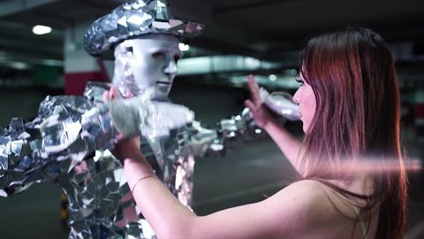 Young man in mirrored suit and mask dancing with ballerina in the underground parking 4K