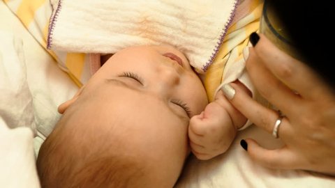 Mum feeds with a spoon her cute newborn baby puree of zucchini closeup