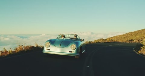 Happy couple driving on country road into the sunset in classic vintage sports car