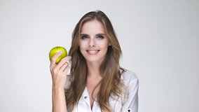 Smiling attractive woman in white shirt eating green apple