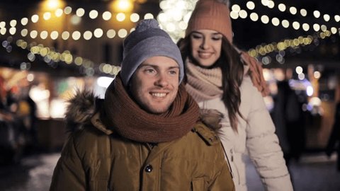 love, winter holidays and people concept - happy young couple dating and hugging at christmas market in evening