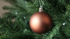 Close-up of matte color bauble hangs on Christmas tree with blinking dot lights 4K 2160p 30fps UltraHD footage - New Year night bronze ball ornament decoration 3840X2160 UHD video