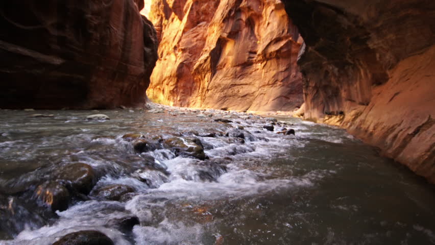View of river flowing through Zion Narrows as canyon glows.
