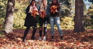 4k, slow motion clip of three girls throwing leaves into the air in a beautiful colorful fall forest setting.  Asian, African american and Caucasian.  Beautiful picture of racial unity.