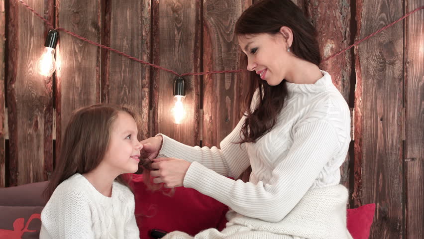 Young mother in white sweater plaiting her daughter hair