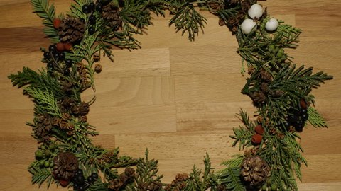 Stop motion of branches, cones and berries of pine trees collecting into a decorative wreath for holidays on a wooden surface