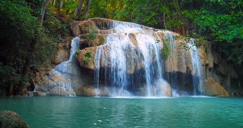 Serene and remote Erawan waterfall in tropical rain forest flows in emerald pond