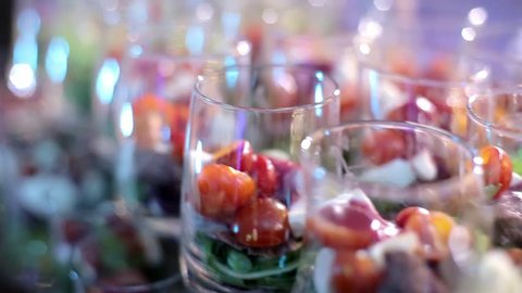 Catering for party. Close up of appetizers with cherry tomatoes, green olives, olive oil, cheese and spices in short glasses on wood brown table. Horizontal color image.