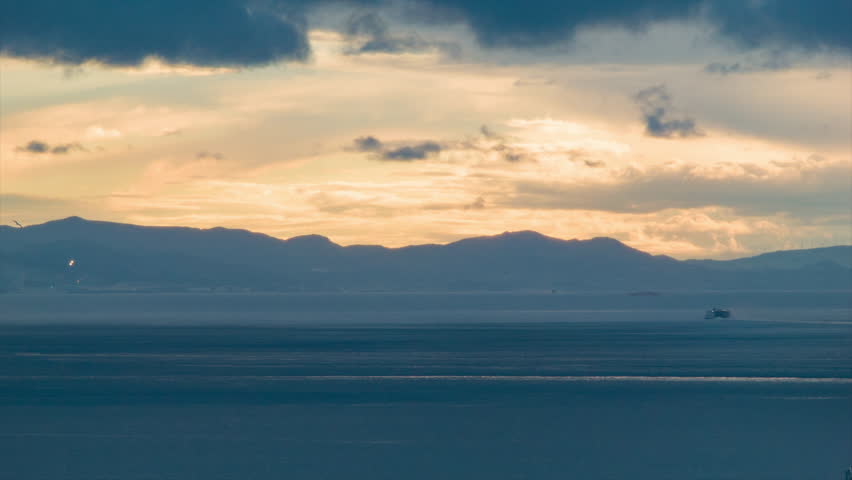 Strait of Gibraltar Sunset Timelapse with Passing Ships and Orange Sun Colored Moving Clouds and a Mountain Range of Morocco in the Background