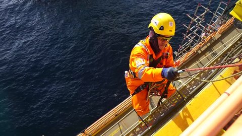 KELANTAN, MALAYSIA - JAN 10 2016 : Man working overboard. Abseiler complete with personal protective equipment (PPE) climbing and hanging at the edge of oil and gas rig platform in the middle of sea.