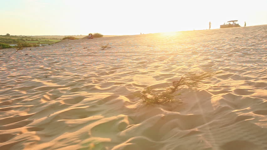 caucasian small blond girl with pigtail runs walks barefooted on sand dunes stops tired comes back at sunset